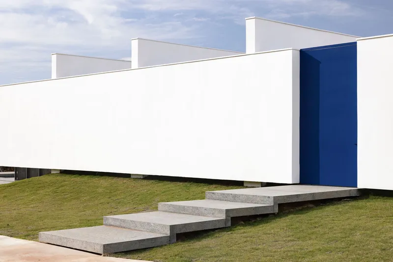 Floating granite stair treads ascending a grass lawn toward white volumes and a blue accent wall