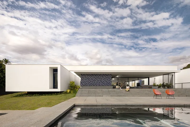 Pool terrace with reflecting water facing white volumes and patterned screen wall under cloudy sky