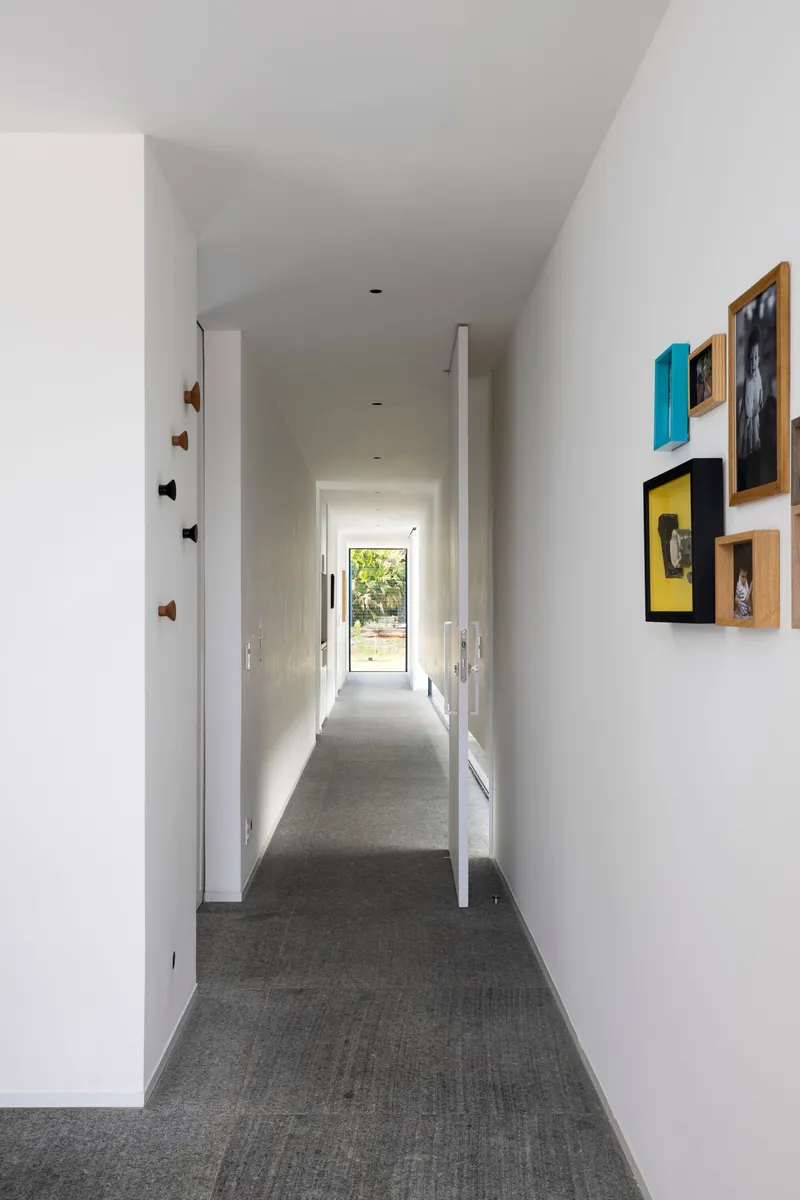 White corridor with framed photographs on one wall leading to distant glazed door and garden view