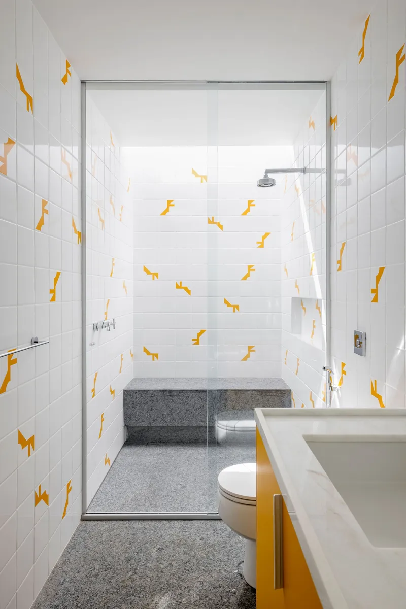 Bathroom with glass shower enclosure, yellow vanity base, and white tiles with yellow animal-shaped decals