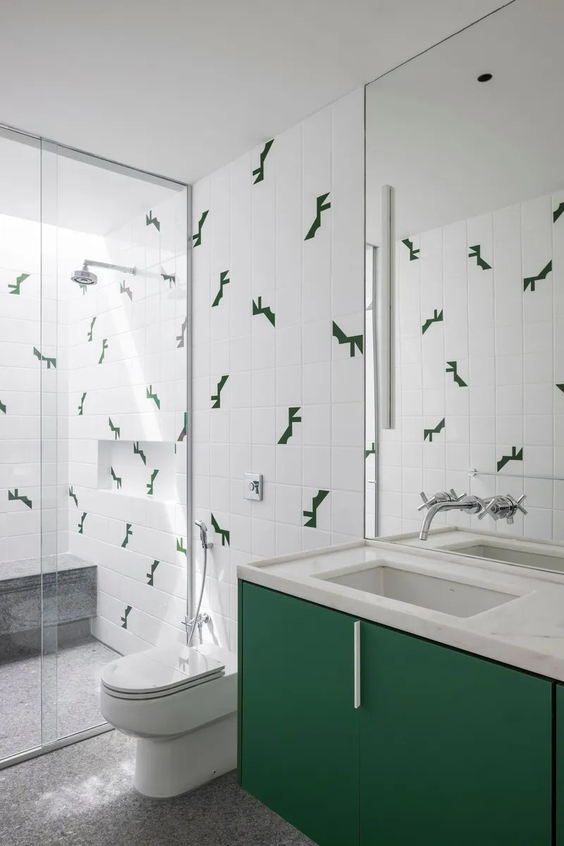 Bathroom with green vanity cabinetry, white tiled walls decorated with dark green geometric decals, and terrazzo flooring