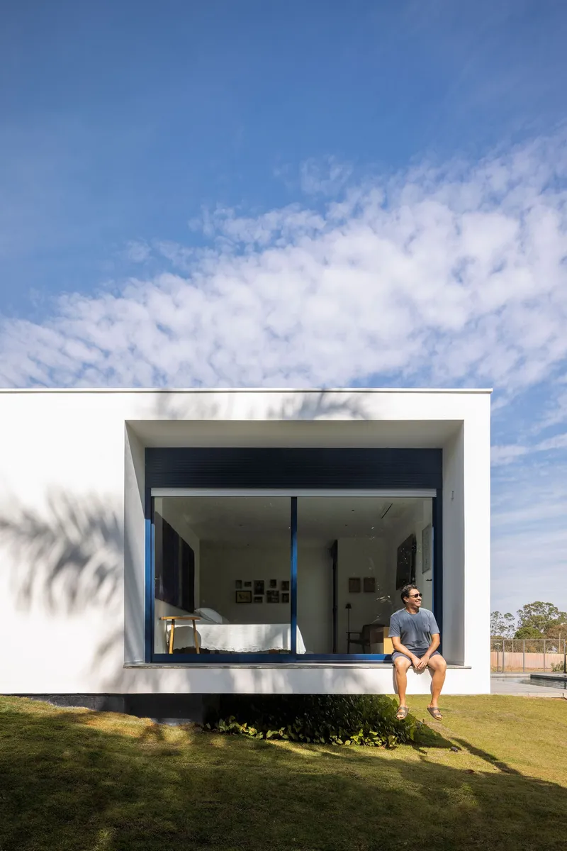 White cantilevered volume with glazed opening and seated figure under a blue sky with scattered clouds