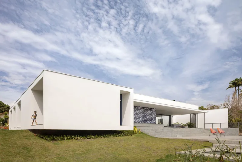 White single-story residence with cantilevered wings across a grassy slope under cirrus clouds