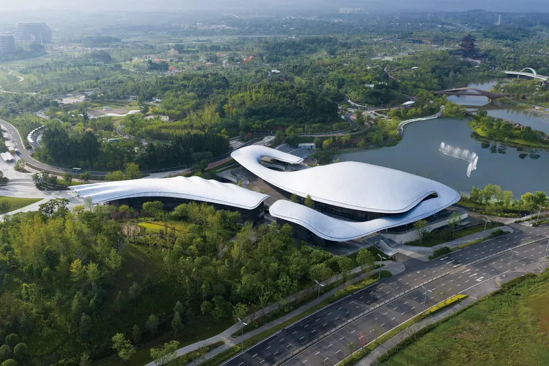 Aerial view of the undulating white roof nestled between dense green forest and a lake