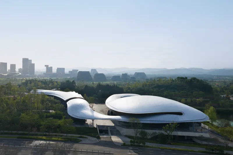 Elevated perspective showing the curved roof volumes against a backdrop of distant mountains and haze