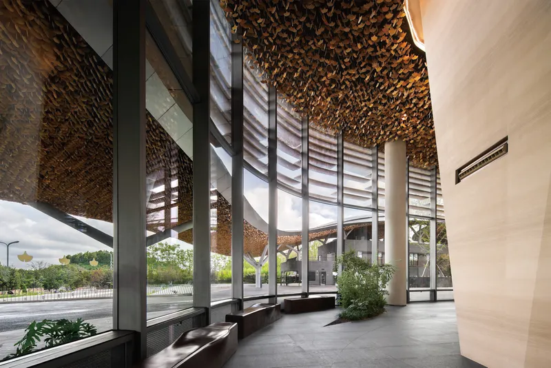 Interior lobby with glass curtain walls, louvered screens, and golden ceiling beneath the canopy