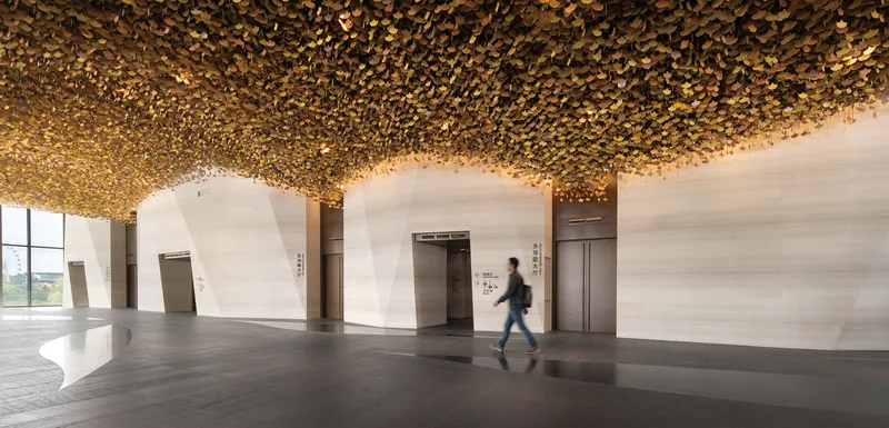 Elevator lobby with textured golden ceiling and pale stone walls as a figure passes by