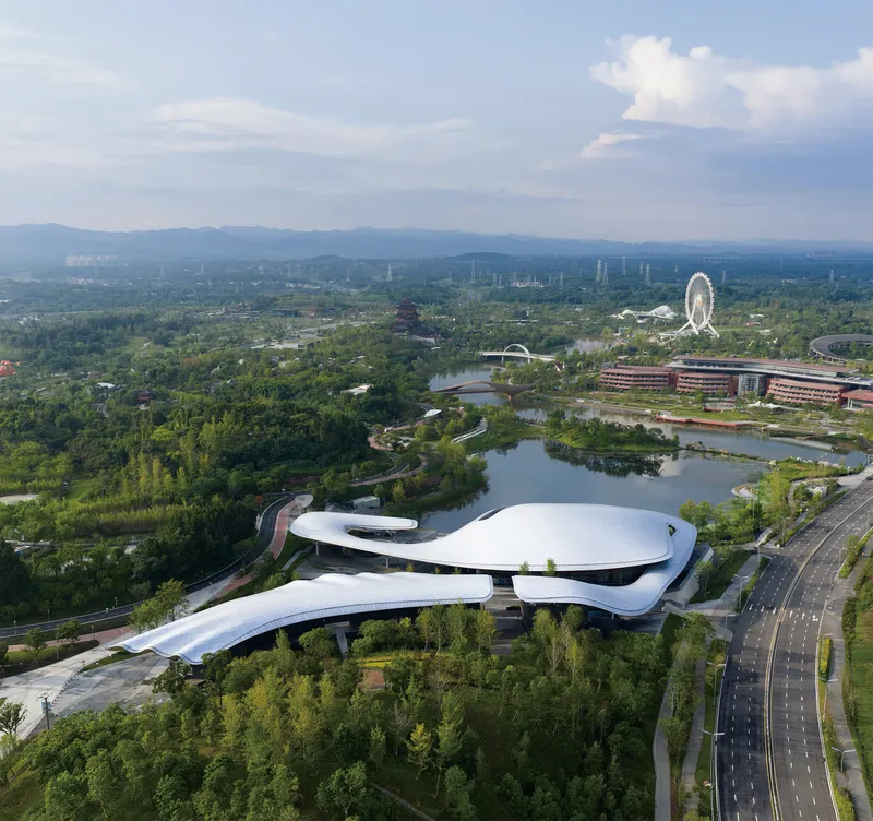 Aerial view of the curved white roof surrounded by parkland and waterways under afternoon clouds