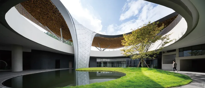 Interior courtyard with circular reflecting pool, lawn, and curved roof canopy overhead with planted soffit
