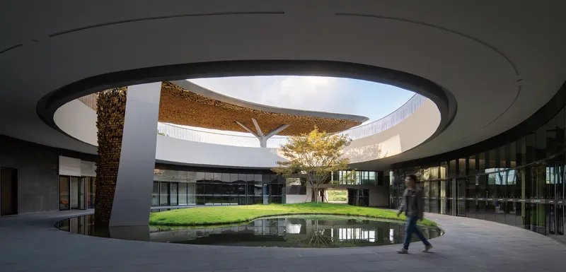Circular oculus framing the central courtyard as a figure walks beneath the cantilevered roof edge