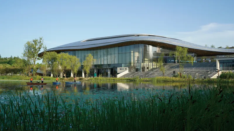 Glass curtain wall and curved roof reflected in a pond edged with tall grasses and visitors