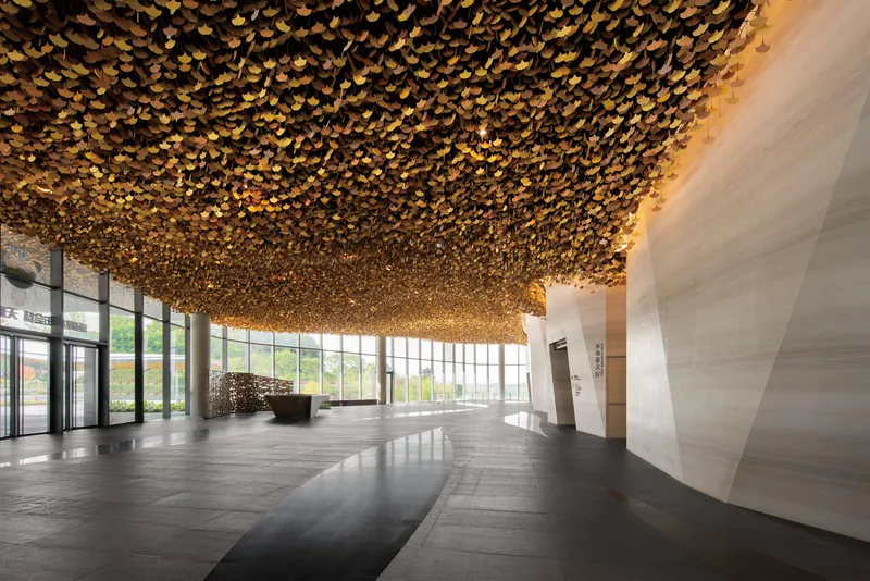 Interior lobby with textured golden ceiling installation above dark stone floors and white angled walls