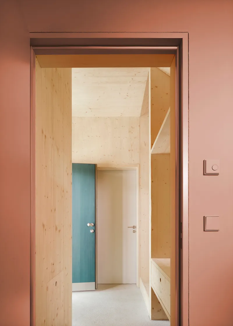 Doorway in a pink wall opening to a light wood corridor with blue and white doors