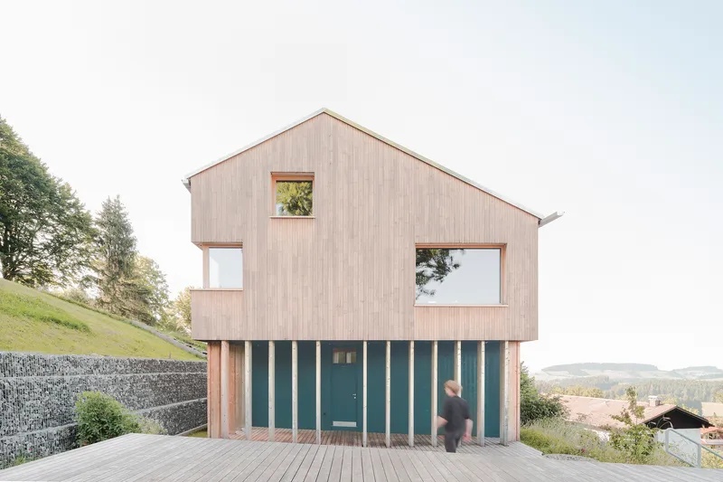 Vertical timber-clad facade with vertical slatted screen at ground level and a figure crossing the terrace