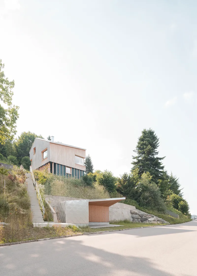 Hillside street view showing timber-clad upper volume on slats above concrete lower garage with slatted door