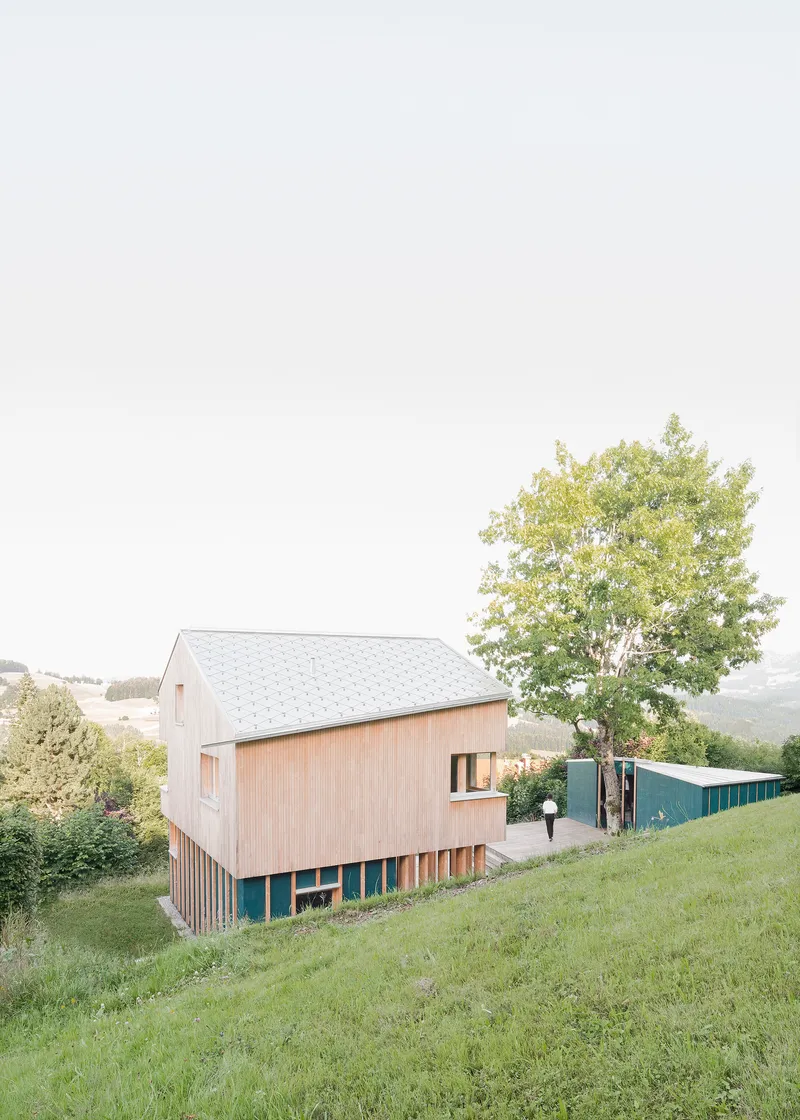 Side view of the timber-clad gabled volume elevated on vertical slats above a grassy slope