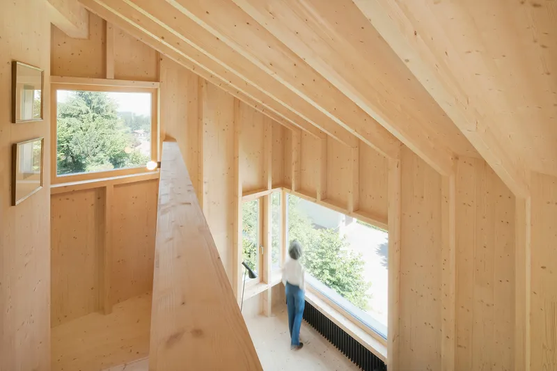 Upper-level interior hallway with exposed timber framing and person standing at window overlooking landscape