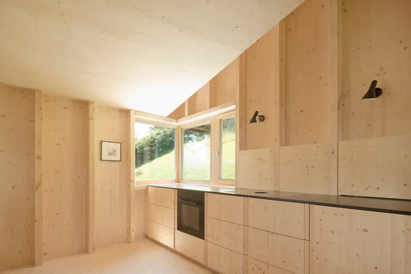 Kitchen interior with exposed timber walls and clerestory window framing view of grassy hillside