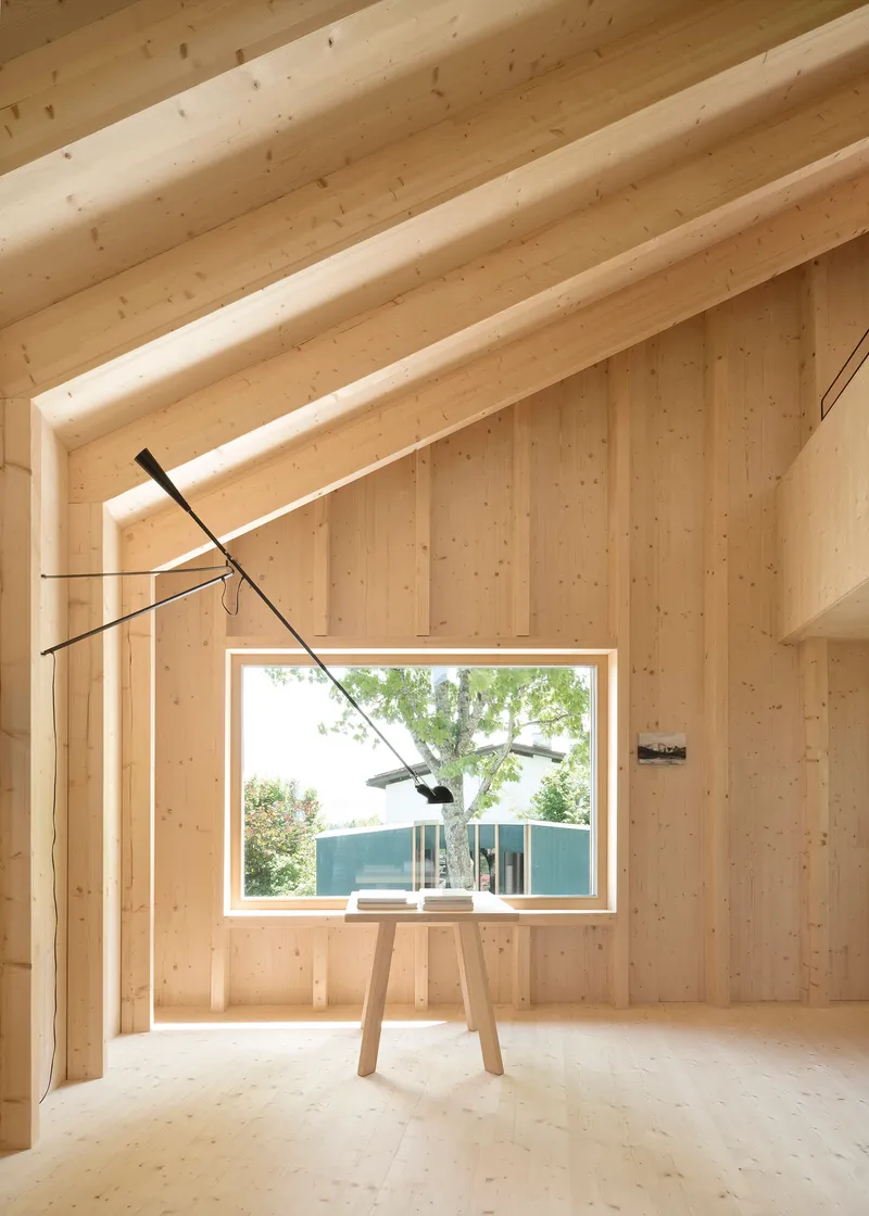 Double-height timber-lined room with picture window framing blue pavilion and cantilevered black pendant fixture