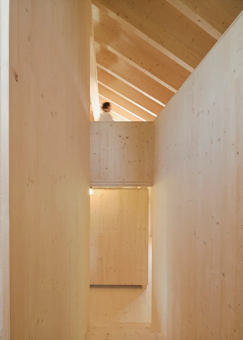 Light wood stairwell with exposed beams and a figure ascending beneath the pitched roof