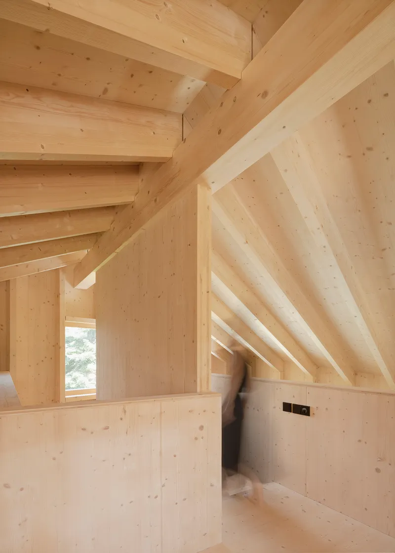 Interior room with exposed timber rafters and light wood walls with a blurred figure walking