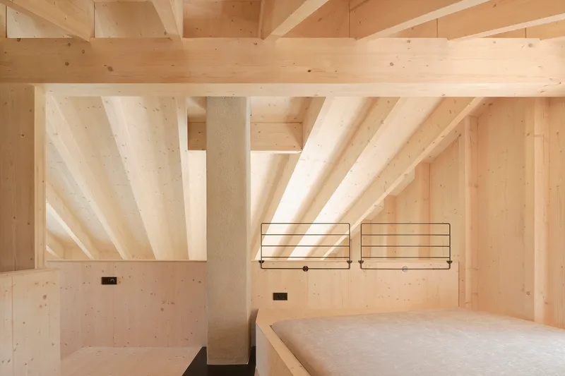 Bedroom with exposed timber beams, light wood walls and minimal steel frame bedside fixtures