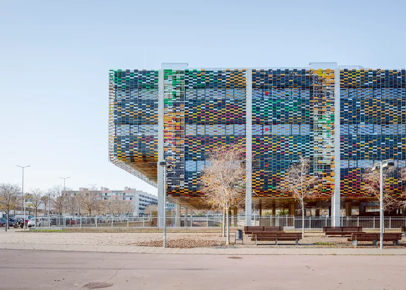 Long facade showing the pixelated screen with white structural columns and bare winter trees in foreground