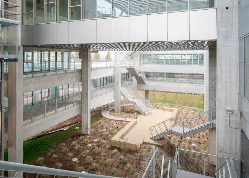Interior courtyard with planted beds, walkways and stairs beneath a patterned metal canopy overhead