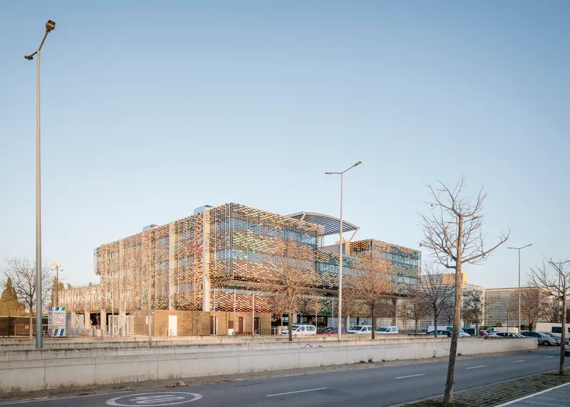 Street view showing the cantilevered volume with multi-coloured screen and bare trees in winter light