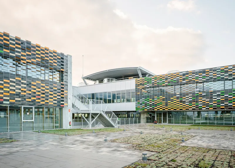 Courtyard view of white bridge linking buildings with multi-coloured screen facades under cloudy sky