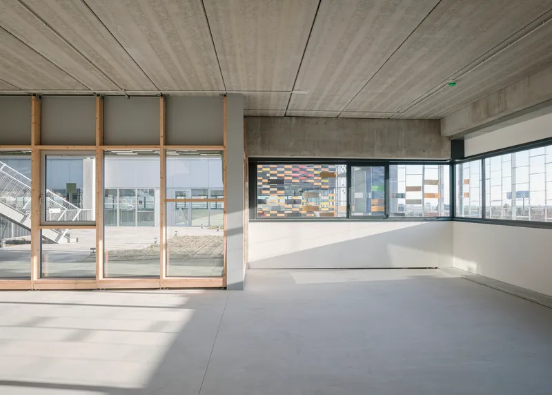 Interior space with board-formed concrete ceiling and floor-to-ceiling glazing overlooking the perforated ceramic facade