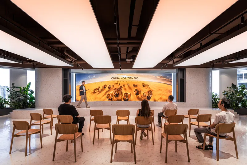 Wooden chairs arranged in rows facing a large illuminated photographic mural with people seated