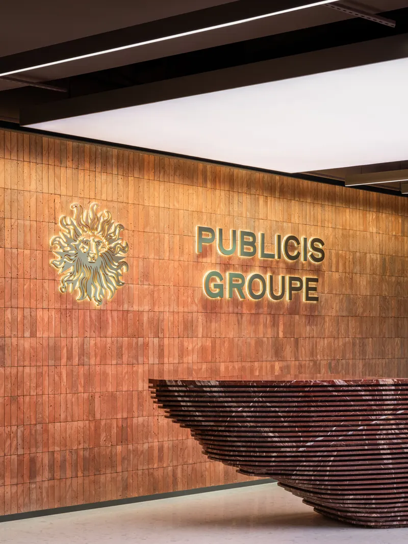 Timber-clad reception wall with brass lettering and a sculptural woven reception desk under linear ceiling lighting