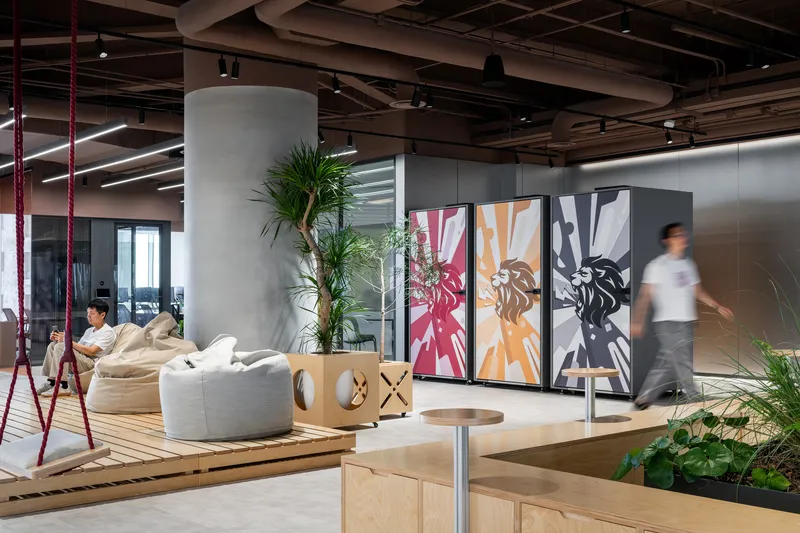Open office lounge with concrete column, triptych panels and a person walking past timber platform seating