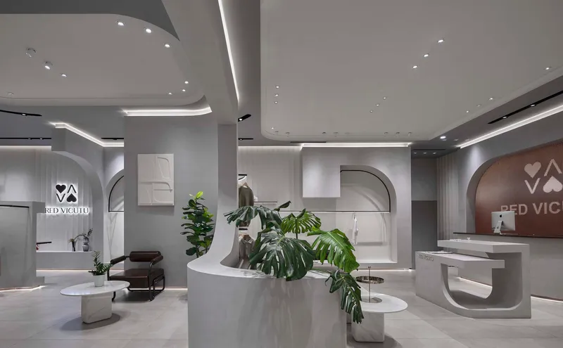 Open retail floor with curved display platforms, recessed cove lighting and potted greenery throughout