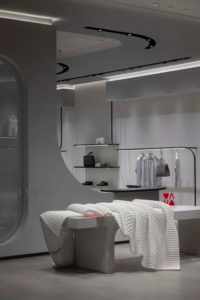 Display area with black curved ceiling track, glass shelving and upholstered seating in foreground