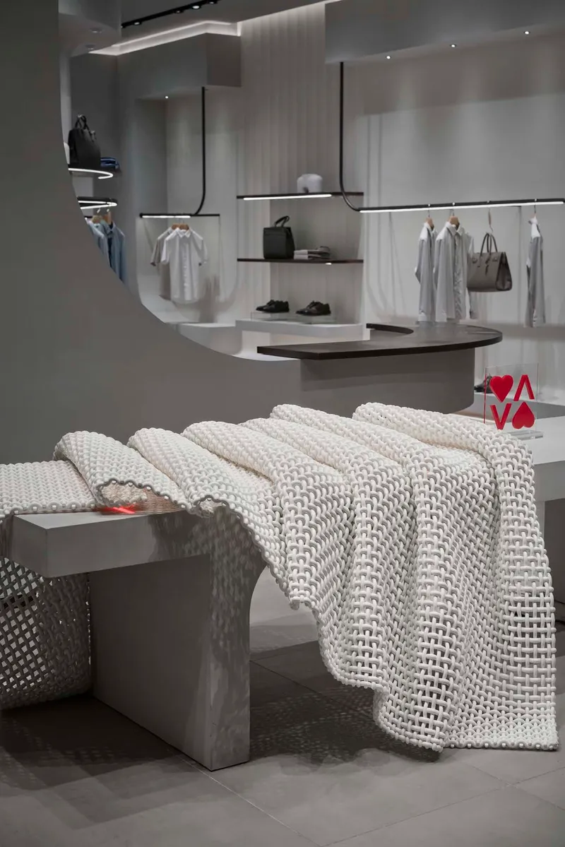 Retail interior with concrete bench draped in white knitted textile under linear ceiling lighting