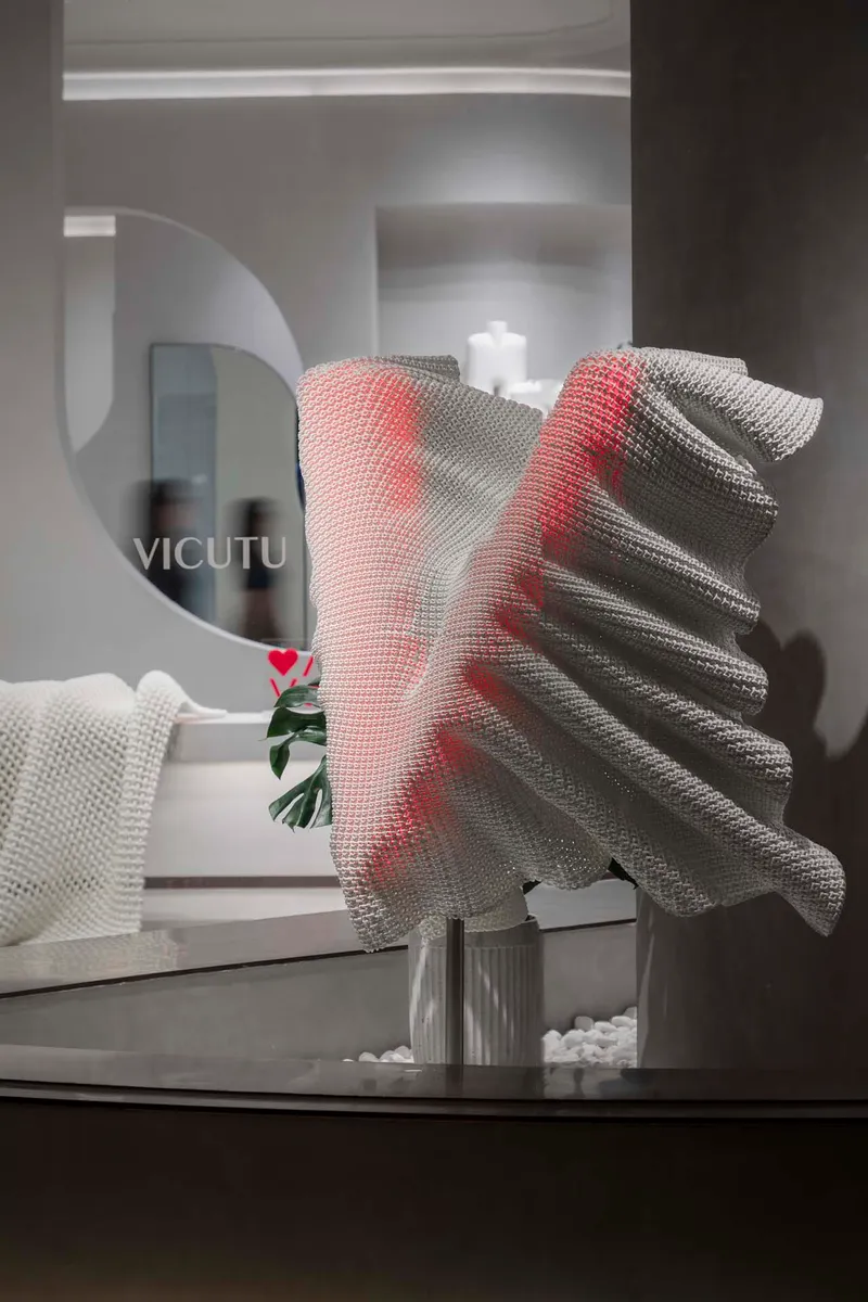 Close-up of red and grey mesh fabric sculpture on glass table beside circular mirror