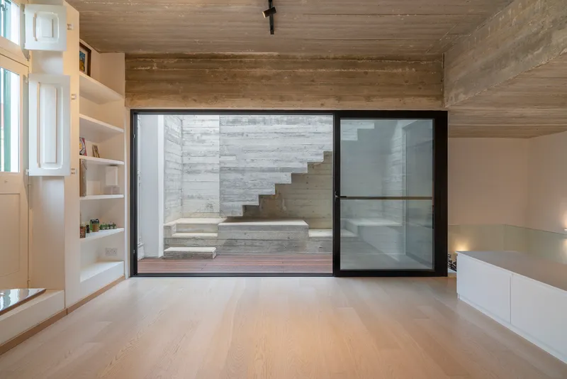 Interior living space with board-formed concrete ceiling and glazed wall framing a cantilevered exterior staircase