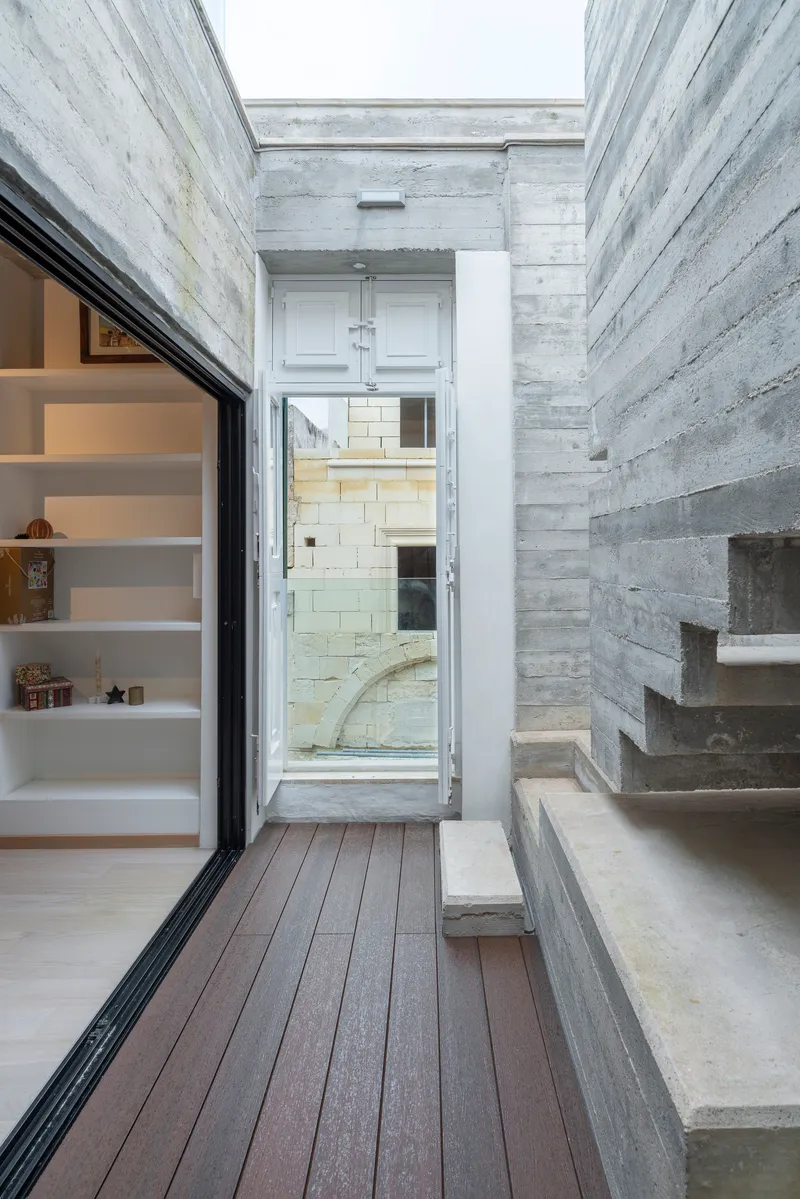 Open-air courtyard with board-formed concrete walls, timber decking, and cantilevered concrete stairs under a skylight
