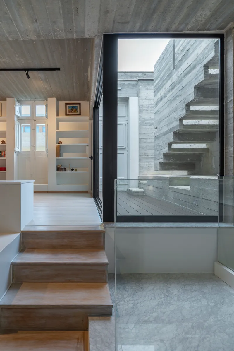 Internal timber stair connecting to exterior courtyard with cantilevered concrete steps beyond glazed black-framed doors