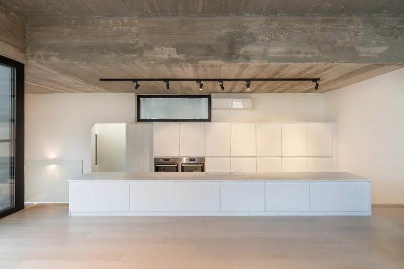 Kitchen with white island and wall cabinetry below board-formed concrete ceiling and black track lighting