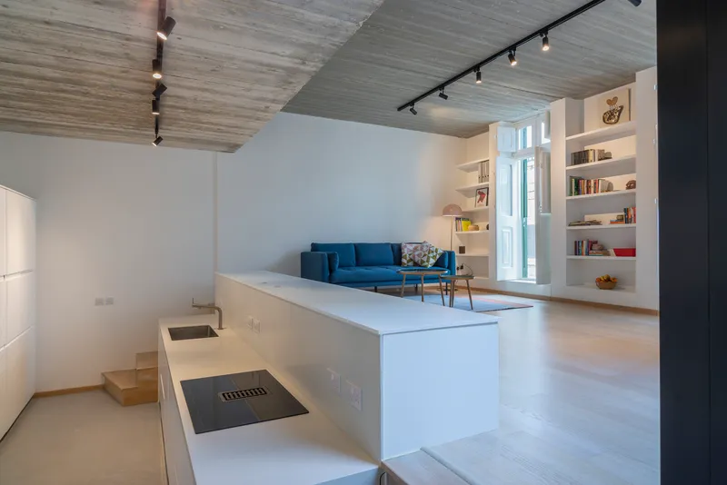 Open-plan living area with blue sofa, built-in shelving, and board-formed concrete ceiling under track lighting