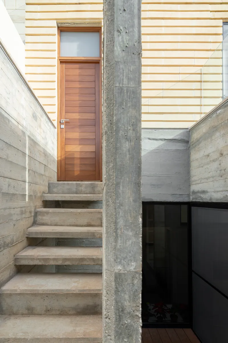 Concrete stairs leading up to a wooden door flanked by board-formed concrete walls and a weathered column