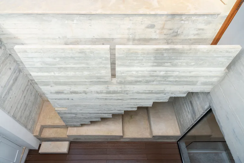 Overhead view of concrete stairs beneath a board-formed ceiling with natural light filtering through
