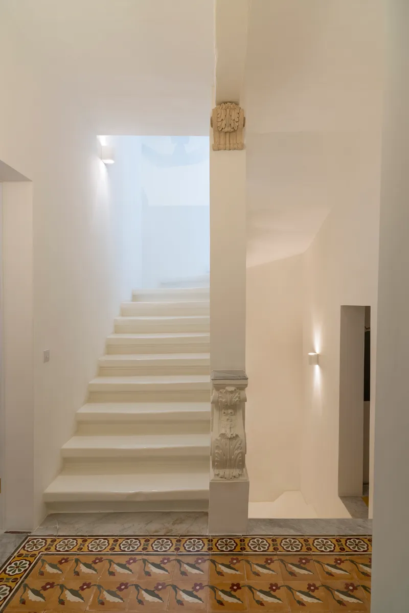 White plastered staircase with carved stone balustrade above decorative patterned floor tiles