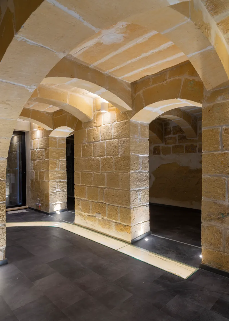 Vaulted sandstone corridor with exposed masonry walls and recessed floor lighting at night