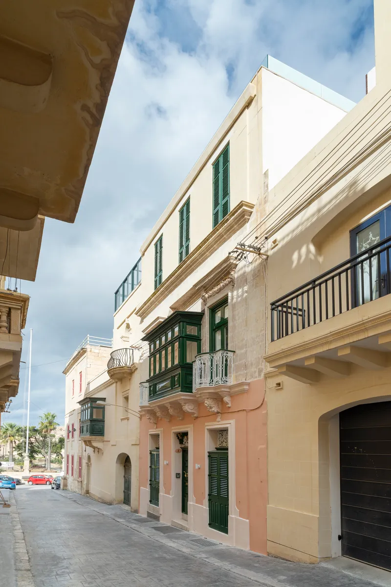 Street view of limestone facades with green shuttered windows and wrought iron balconies