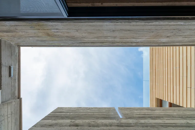Upward view framed by board-formed concrete beams with timber cladding against the sky