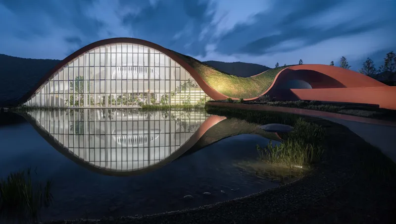 Glass-walled facade with arched roof reflected in still pond at twilight beneath forested hillside